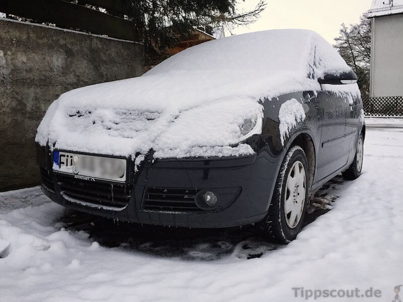 Person kehrt vom Dach eines Autos mit einem Besen den Schnee ab